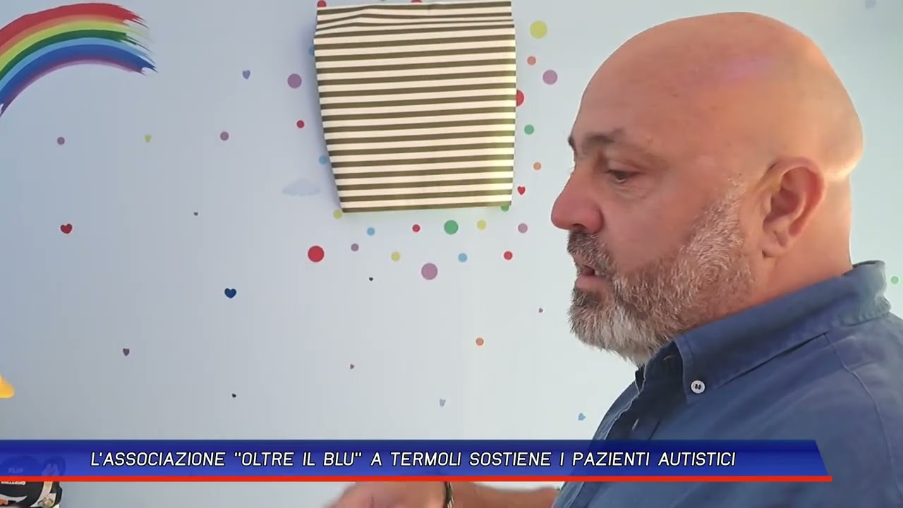 Fotogramma del servizio televisivo: un uomo intervistato di profilo, davanti alla parete dipinta con l'arcobaleno e i pallini colorati della sede
